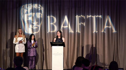 A woman stands at a lectern making an acceptance speech for an award, with the BAFTA logo behind her.