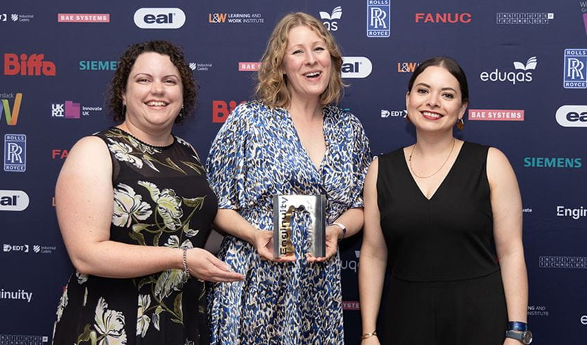 Three women holding an award stood in front of a board branded with company logos