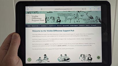 Person holding a tablet computer displaying the website Visible Difference Support Hub