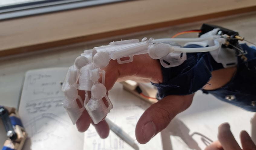 A close up picture shows an exoskeletal bionic glove covering a hand.