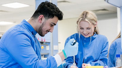 Two students wearing scrubs while working in a lab.