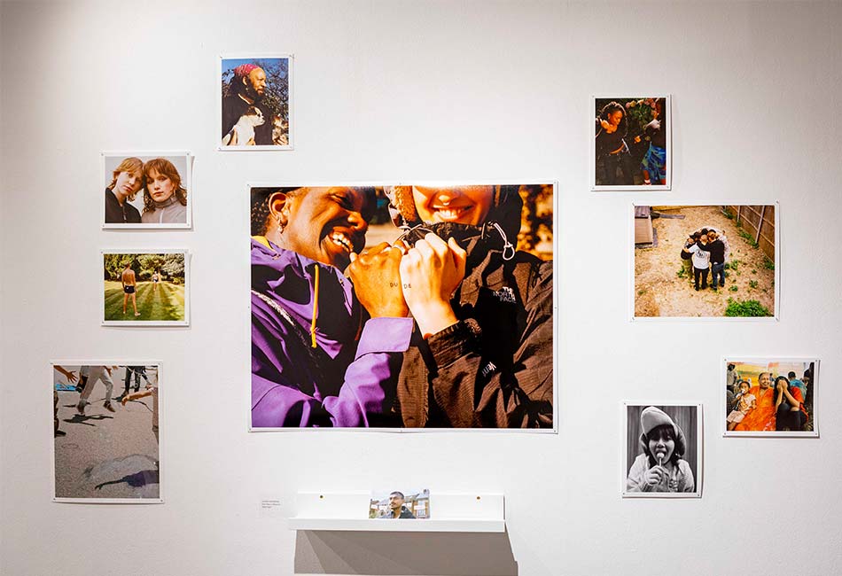 An exhibition wall with photos displayed on it. The central image has two people with their hands together so that 'dude' can be seen written across them.