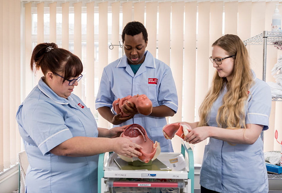 Three midwifery students practice how to support women in giving birth and taking care of newborn babies.