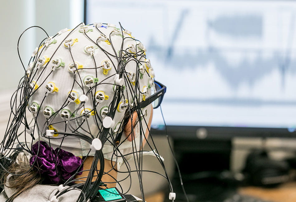 A person wearing electronic sensors on their head while looking at a computer screen.