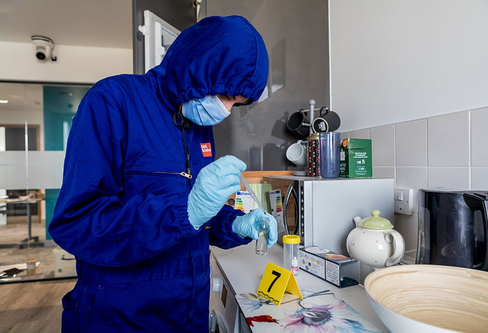 A person wearing dark blue uniform and protective gloves while examining a crime scene in a kitchen.