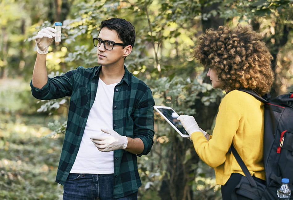 Two students examining and taking samples in a forest.