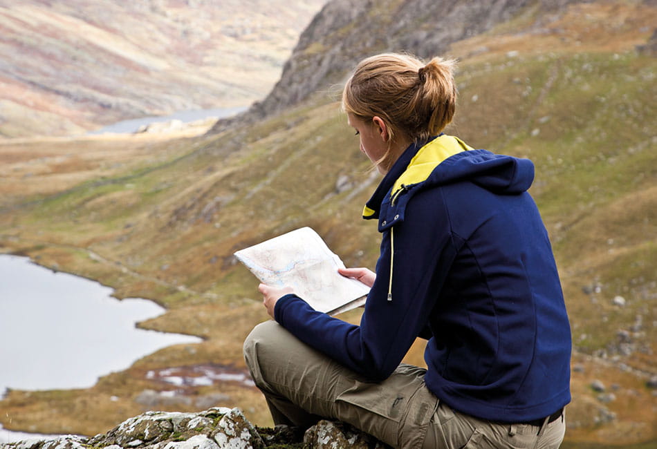 A person sitting by a lake and reading a map.