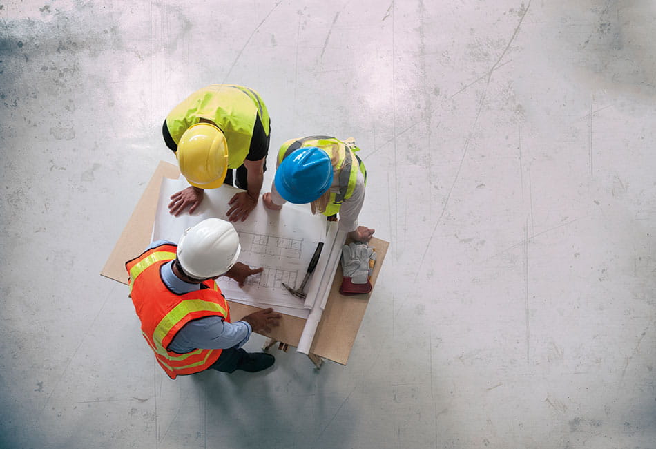 Three construction workers leaning over a table to discuss a plan document.