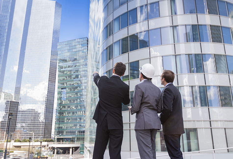 Three people in business suits looking and pointing at tall buildings.