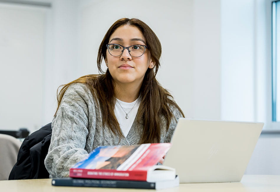 A student studying in a classroom with laptop and a few books.