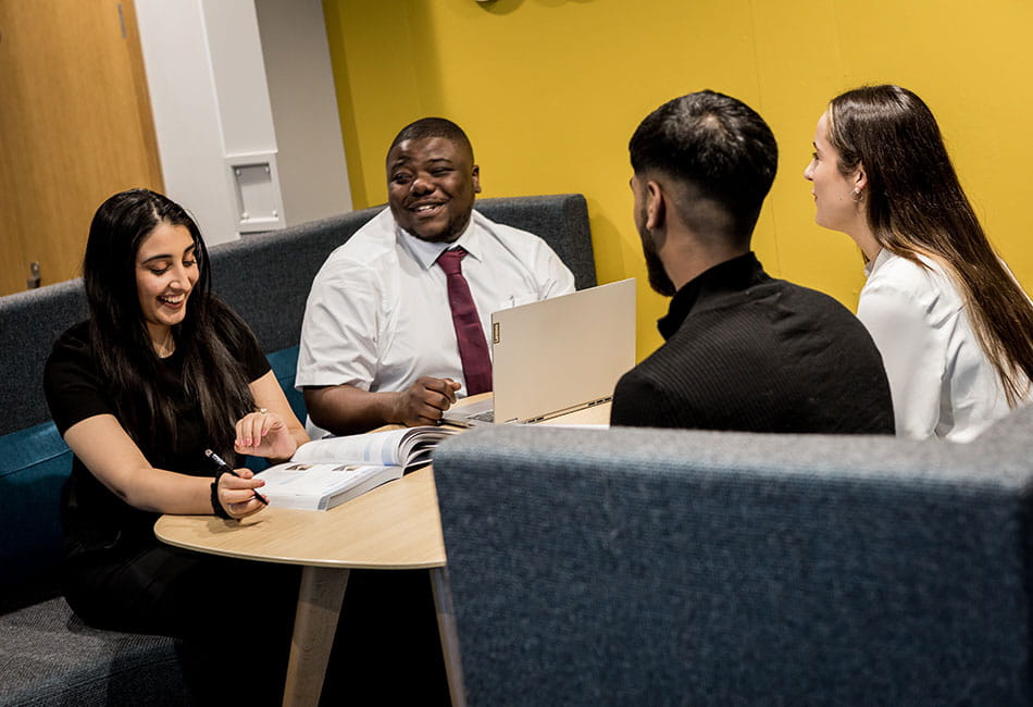 Four students in smart casual outfit having a discussion over their laptops.