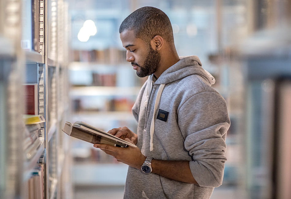 A student standing and reading a book in the library.