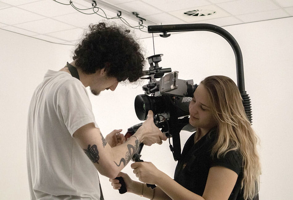 A student inspecting a professional camera whilst another student holds it.