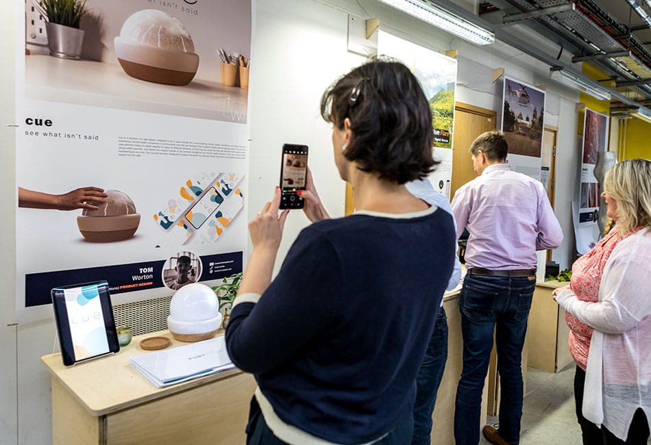 A woman taking a photo of a student's display area at a degree show.