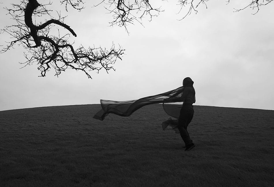 A silhouette of a person with a scarf blowing on a hillside.