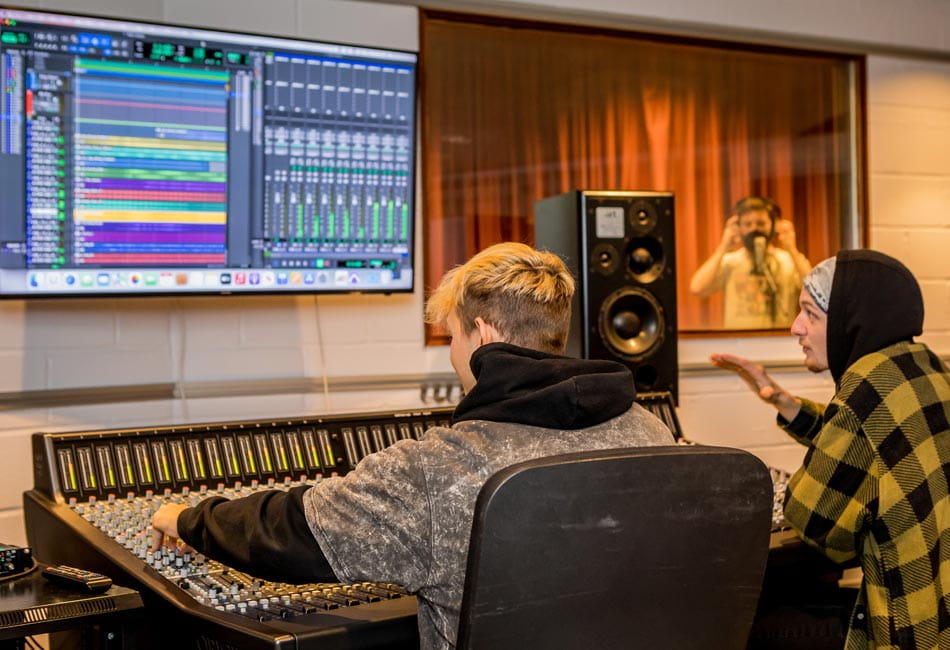 Three students using a mixing desk in a studio.