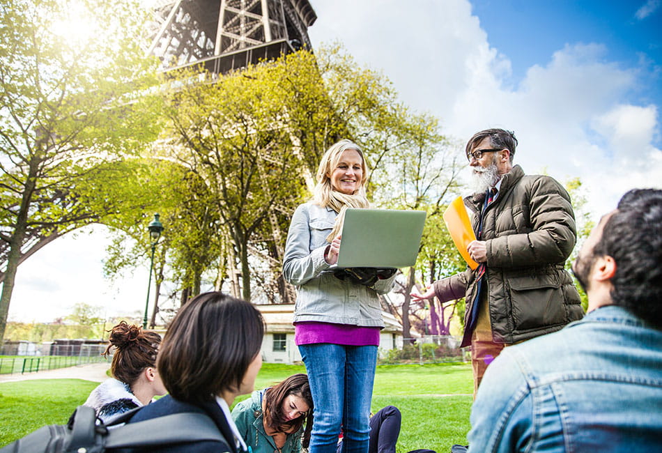 A group of people relaxing and talking near the Eiffel Tower under a sunny blue sky.