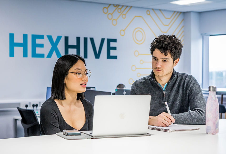 A man talking to a student who is looking at her laptop in an office space.