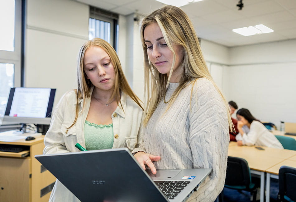 Two students discussing their work while looking at a laptop screen.