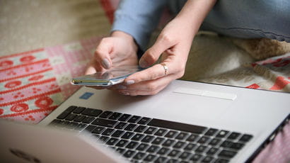 Someone holding a mobile phone in front of a laptop