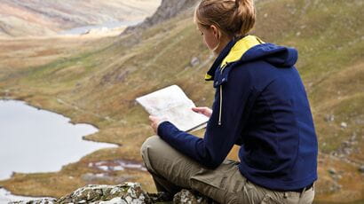 A young hiker reads a map with mountains and lakes in the background. Image credit: Laura Piebinga.