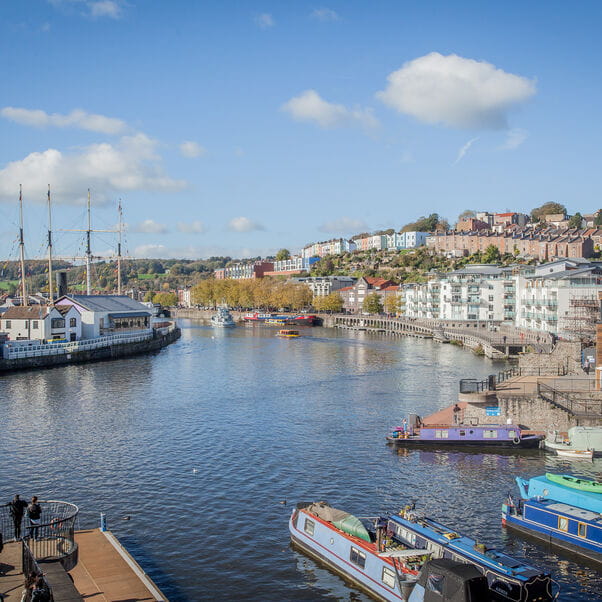 Panoramic view of Bristol harbour' with coloured houses on the hill and boats/ships on the waterfront.