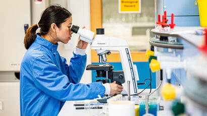Biomedical student looking into a microscope in a lab.
