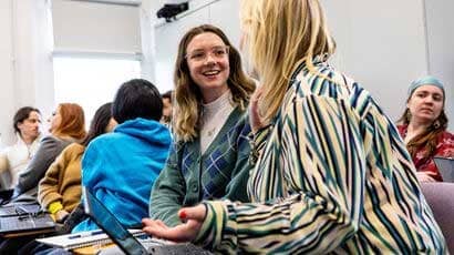 A couple of smiling students talking to each other in a lecture.