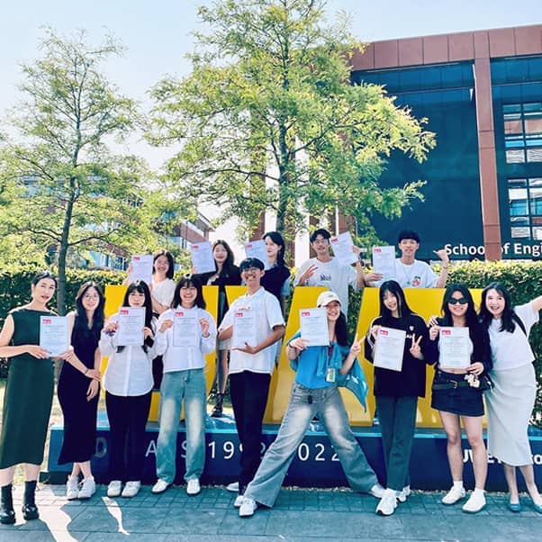 A happy group of International Summer School students posing on the UWE sign at Frenchay Campus.