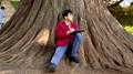 A Summer School student perched at the base of a huge yew tree.
