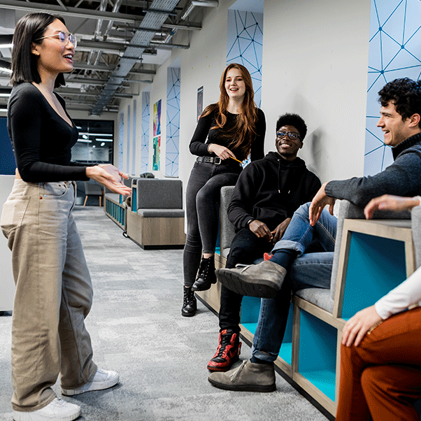 A student talks to a group sitting on comfortable chairs in a collaborative working space on campus.