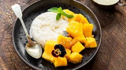 A black ceramic dish containing bright chopped mango and sticky white rice.