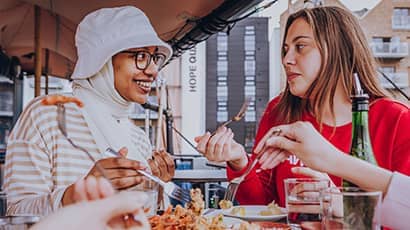 Two students talking at a harbourside restaurant table full of food.
