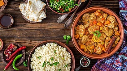 Traditional tajine dishes, couscous and fresh salad on rustic wooden table.
