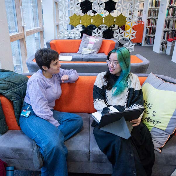 Student sat on a soft with an advisor pointing at a laptop