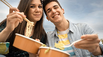 A man and a woman eating noodles with chopsticks.