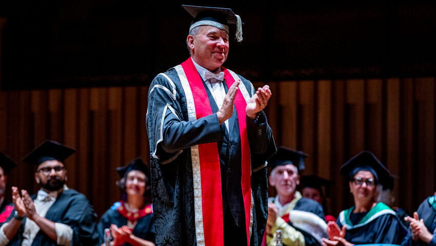 Professor Steve West clapping on stage at the graduation ceremony