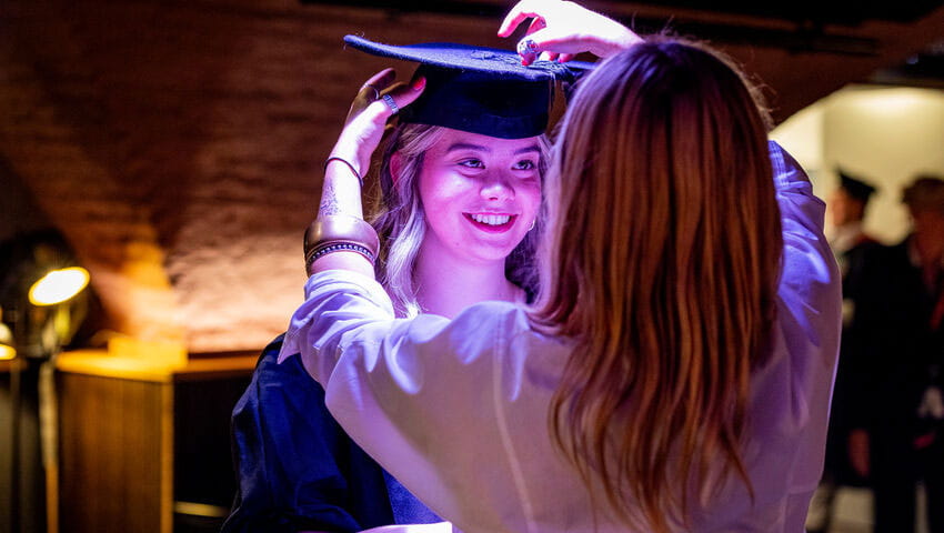 Student getting her graduation robes adjusted by a parent.