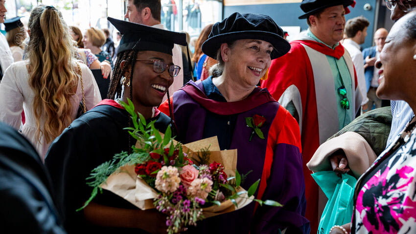 A student graduate holding a bunch of flowers with an academic