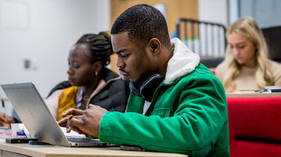 Students sitting in a hall listening to a lecture and taking notes.