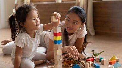 An early years teacher caring for a small child playing with building blocks.