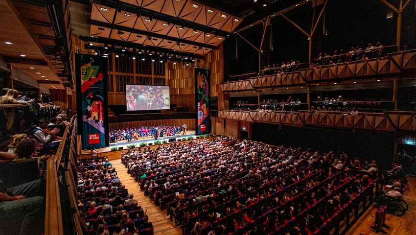 A large auditorium filled with people sat looking towards a stage