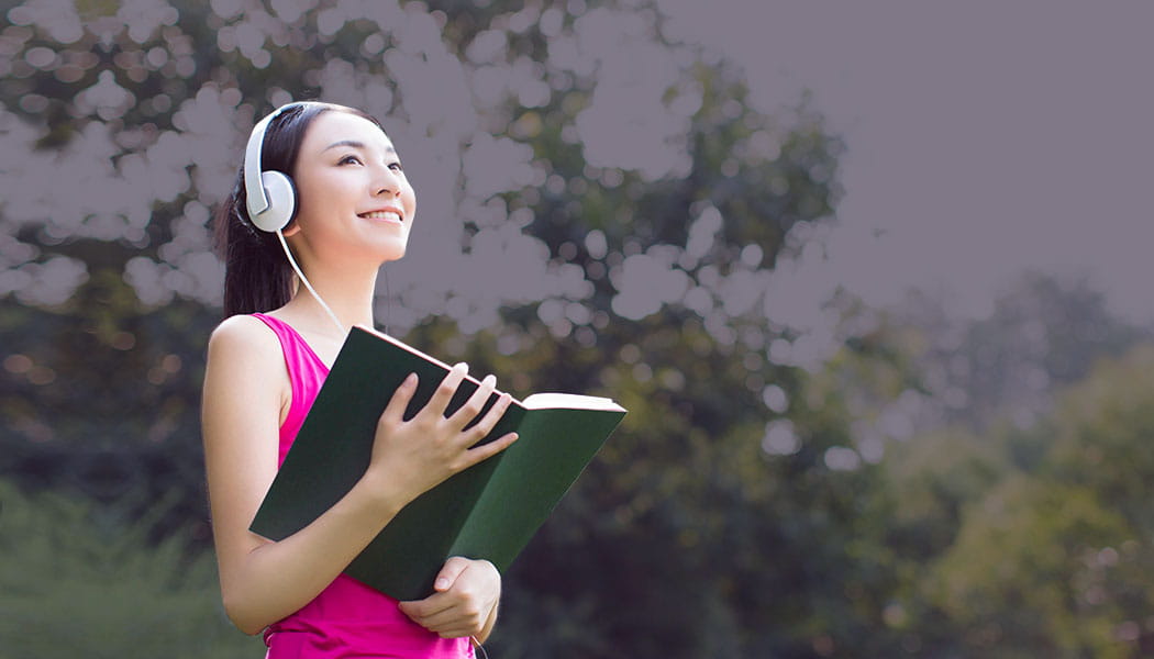 Smiling student wearing headphones with book in hand