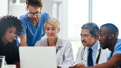 A group of healthcare professionals looking at a laptop.