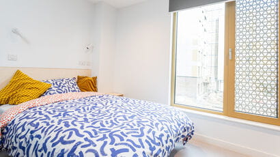 Student room in on-campus accommodation with small double bed and large window.