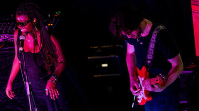 A black woman singing and a white man playing guitar on stage.