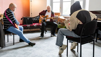 Three white men playing guitar together in a practice room