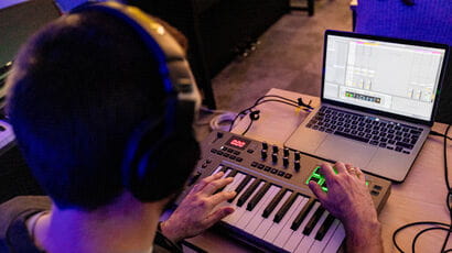 A white man with a laptop and electronic piano keyboard mixing sound.
