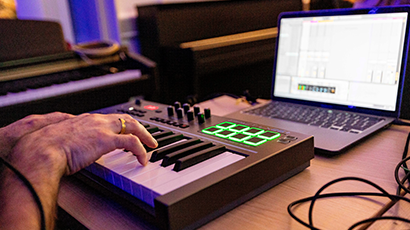 hands at a small keyboard with a laptop screen on the desk