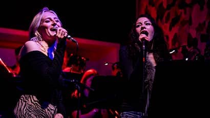 Two women singing into microphones on a stage